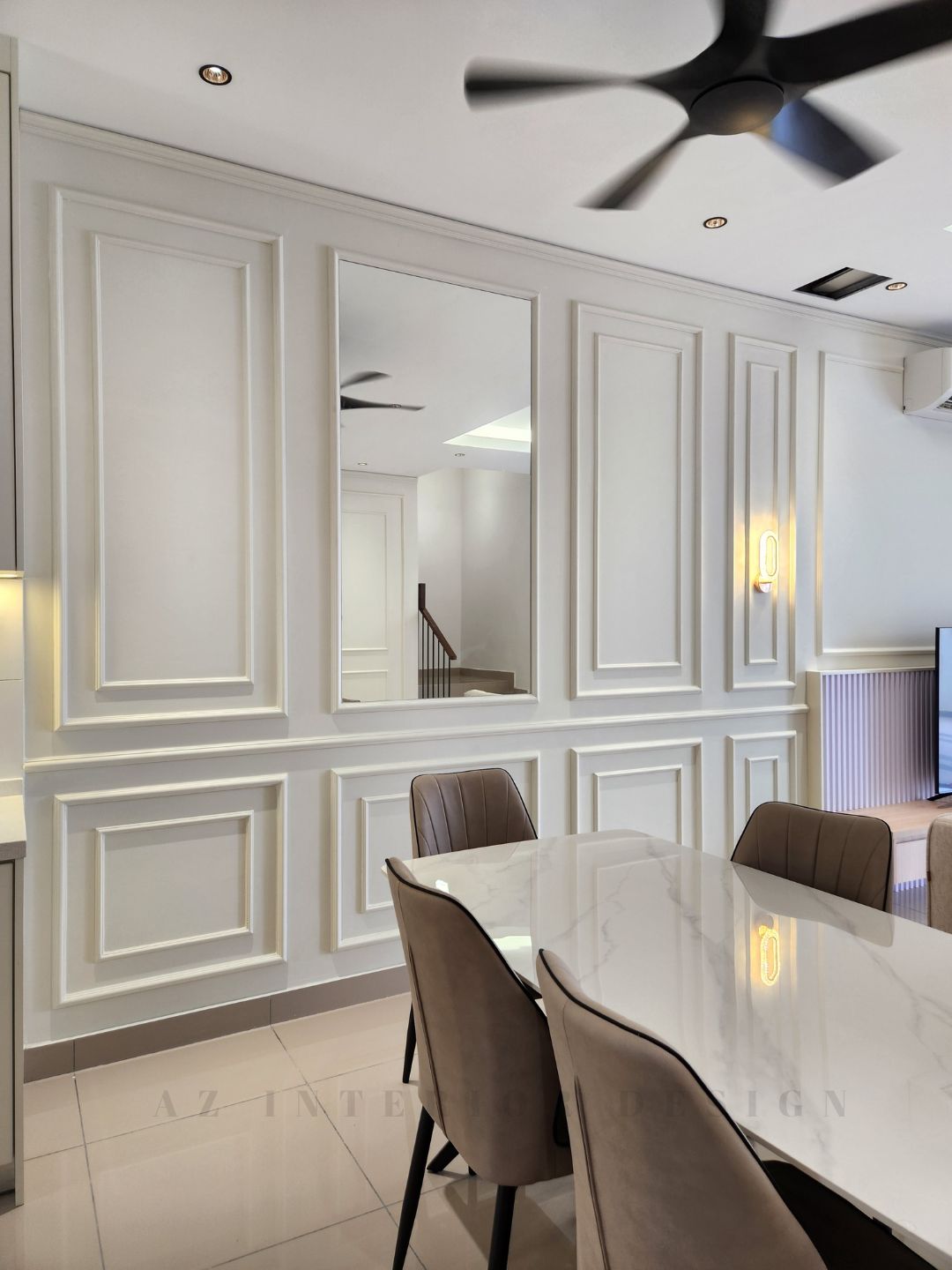 Open-plan living, dining, and kitchen area with classic European wall paneling, neutral-toned furniture, and modern ceiling fans by AZ Interior Design.